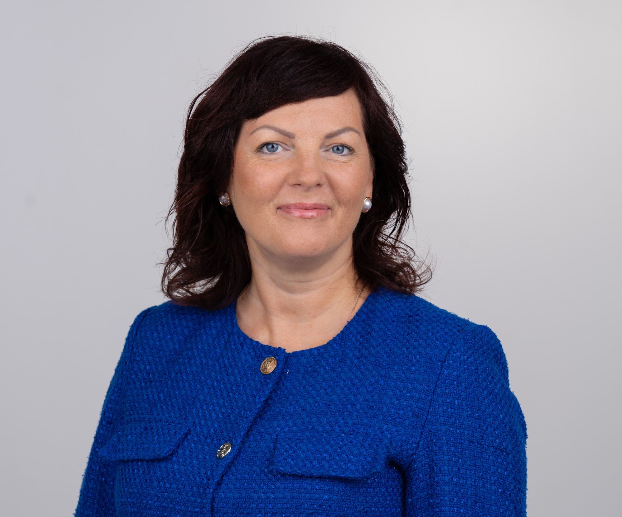 Naine sinises jakis, tumepruunide juuste ja pärlkõrvarõngastega, professionaalne portreefoto.