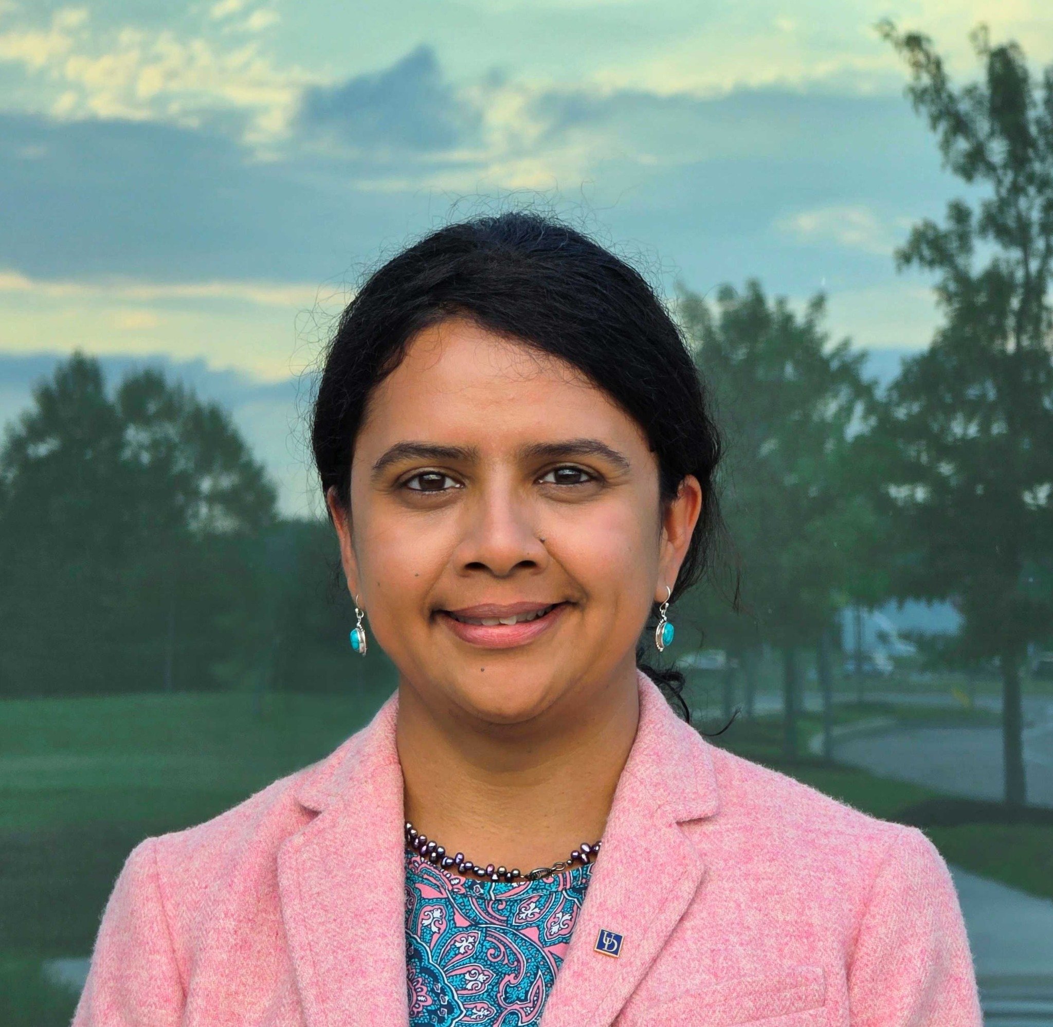 Delaware’i Ülikooli arvutiteadlane Sunita Chandrasekaran roosas pintsakus, taustal puude peegeldused klaasfassaadil.