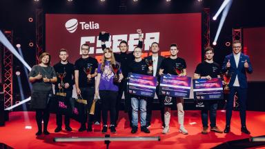 Telia Cyber Battle ja CyberSpike 2025 võistluse võitjad ja auhinnasaajad seisavad punase lava peal trofeede ja auhinnatšekkidega. Taustaks on suur Telia logoga ekraan ning lava on valgustatud professionaalsete valgustega. Võistkonnad kannavad TalTechi ja võistluse särke.