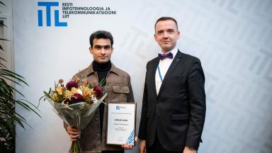 Stipendiumisaaja Junaid Sajid koos lillekimbu ja tunnistusega ning tema kaasjuhendaja Ivo Müürsepp Eesti Infotehnoloogia ja Telekommunikatsiooni Liidu logo taustal. Foto: Joanna Jõhvikas.