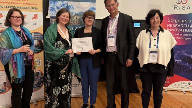 TalTechi IT mitmekesistamise programmi esindajad võtavad vastu Informatics Europe auhinda 21. Euroopa Informaatika Liidrite Tippkohtumisel. Pildil on viis inimest, kes hoiavad käes aukirja Informatics Europe ja IRISA logodega stendide ees.