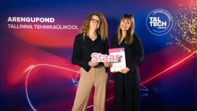 Kaks naist seisavad TalTechi Arengufondi taustaseina ees. Nad hoiavad käes tunnustust ja dokumenti, mis on seotud TalTechi stipendiumiga. Taustal on Tallinna Tehnikaülikooli ja TalTechi Arengufondi visuaalid.