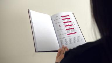 Inimene hoiab käes avatud köidetud magistritööd, mille lehel on skeem.