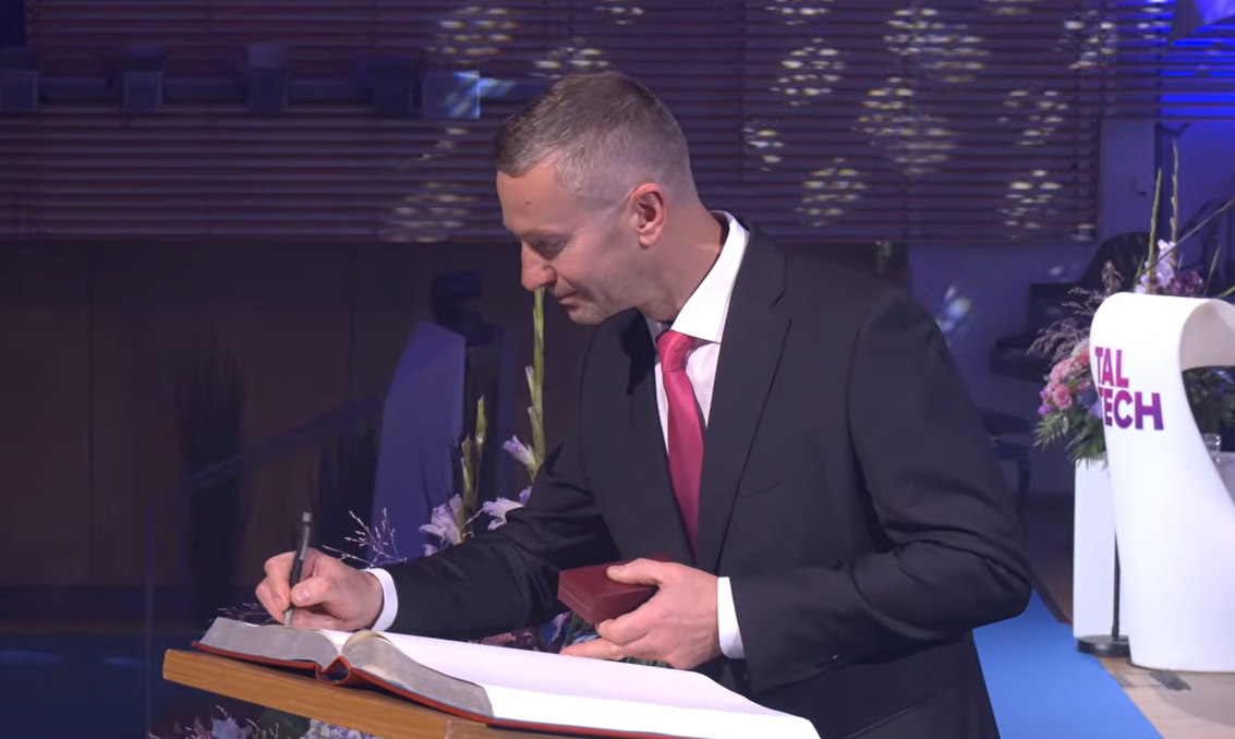 a man in dark suit signing a big book