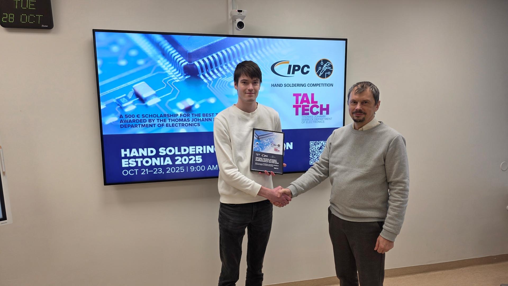 Professor Alar Kuusik annab TalTechi Thomas Johann Seebecki elektroonika instituudi välja pandud 500-eurose stipendiumi elektroonika tudengile Artur Järvanile, taustal ekraanil teave Hand Soldering Estonia 2025 võistluse kohta.