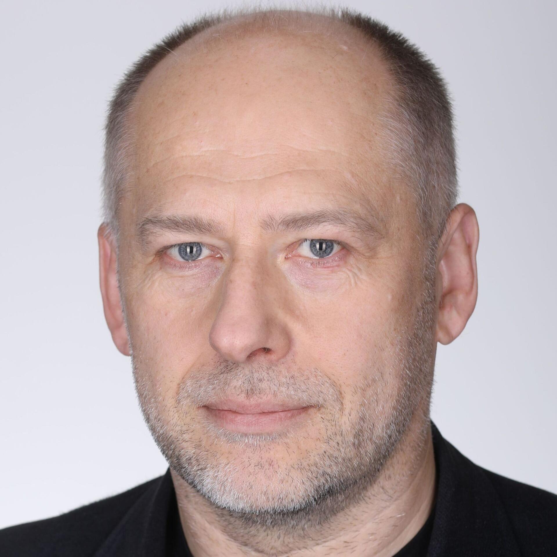 Portreefoto keskealisest mehest, kes vaatab otse kaamerasse. Tal on kiilanev pea, hele nahk ja lühike habe. Seljas on tume jakk ning taust on hele ja neutraalne, sobides ametlikuks profiilipildiks.